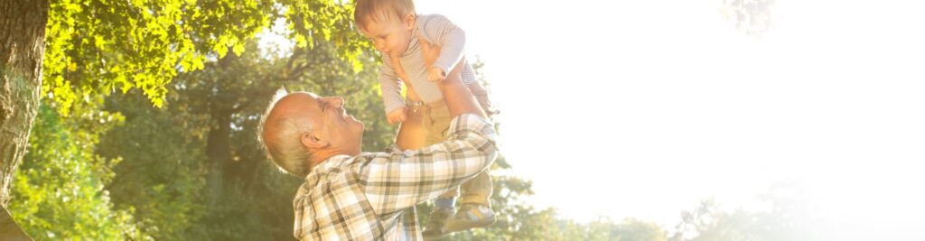 A grandfather playing with his young grandson in a park.